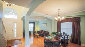 A spacious living room with a dining area, wooden flooring, and a staircase leading to another level. - Enchanted Emerald Oasis by VillaDirect (Kissimmee)