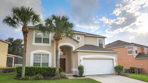 A two-story house with a garage, palm trees, and a well-maintained lawn. - Enchanted Emerald Oasis by VillaDirect (Kissimmee)