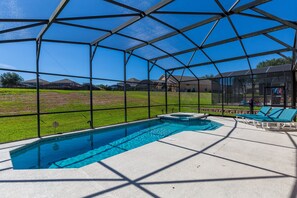 A swimming pool with a glass enclosure, a hot tub, and lounge chairs.