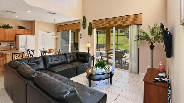 A spacious living area with a black leather sofa, a coffee table with a plant, and a wooden side table with a vase. - Holiday Escape by VilllaDirect (Kissimmee)