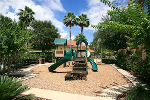 Explore the playground area surrounded by lush trees and a pathway leading to a fun climbing structure and slide.