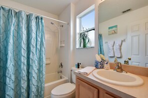 A bathroom with a shower curtain, toilet, sink, and a window with a view of greenery.