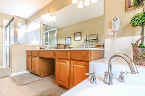 A bathroom with a large mirror, wooden cabinets, a white sink, and a hairdryer mounted on the wall.