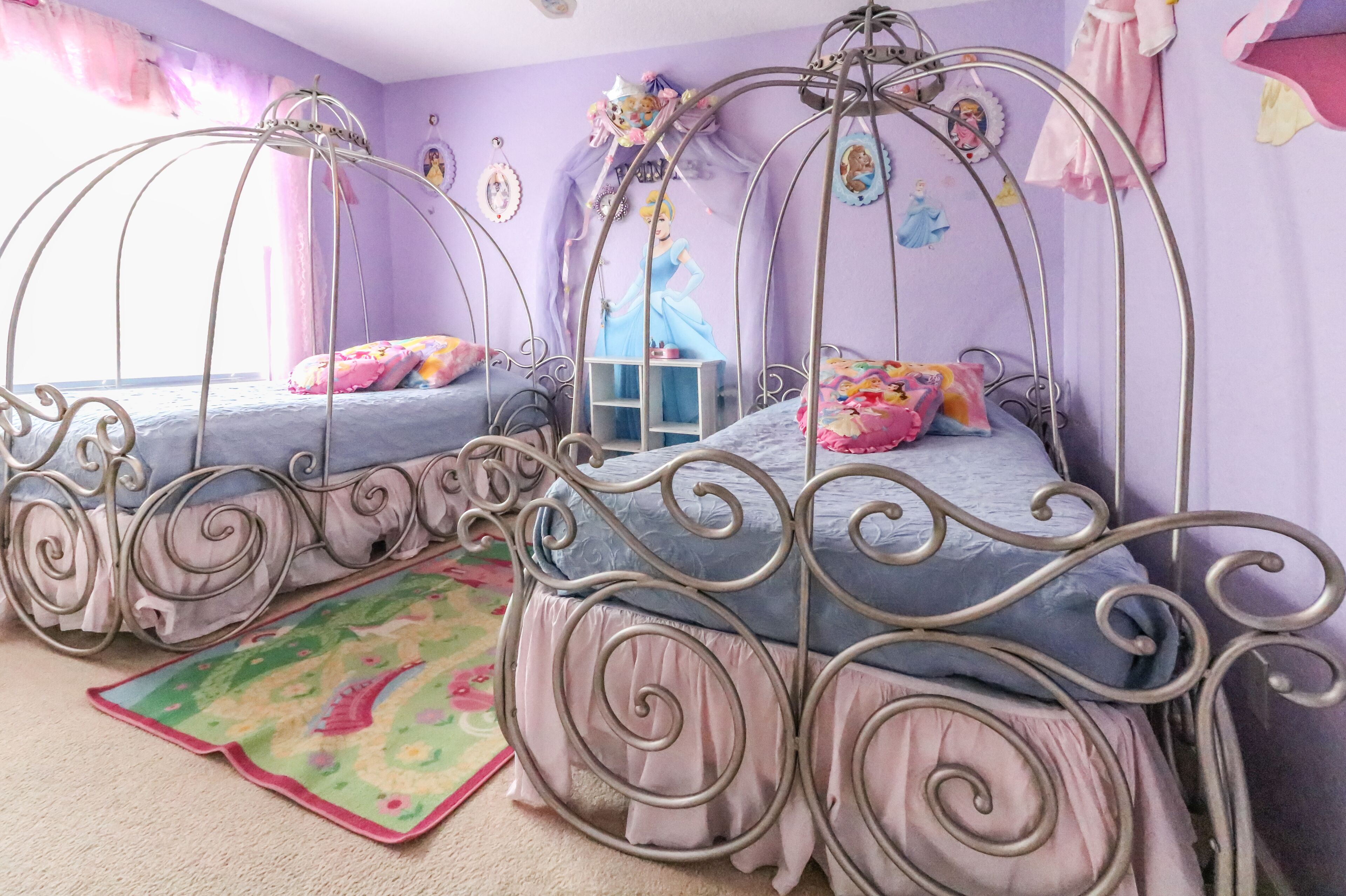 A room with two metal-framed beds with decorative railings, a colorful rug, and wall decorations including a princess mural.