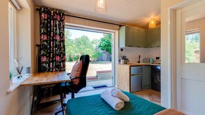 A compact room with a bed, a desk, a chair, a small kitchenette, and a view of the outdoors. - Pass the Keys | Charming and Central Garden Studio Flat | Free Parking (Cambridge)