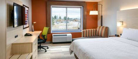 A hotel room with a bed, desk, chair, TV, air conditioning unit, and a window with a view of a construction site.