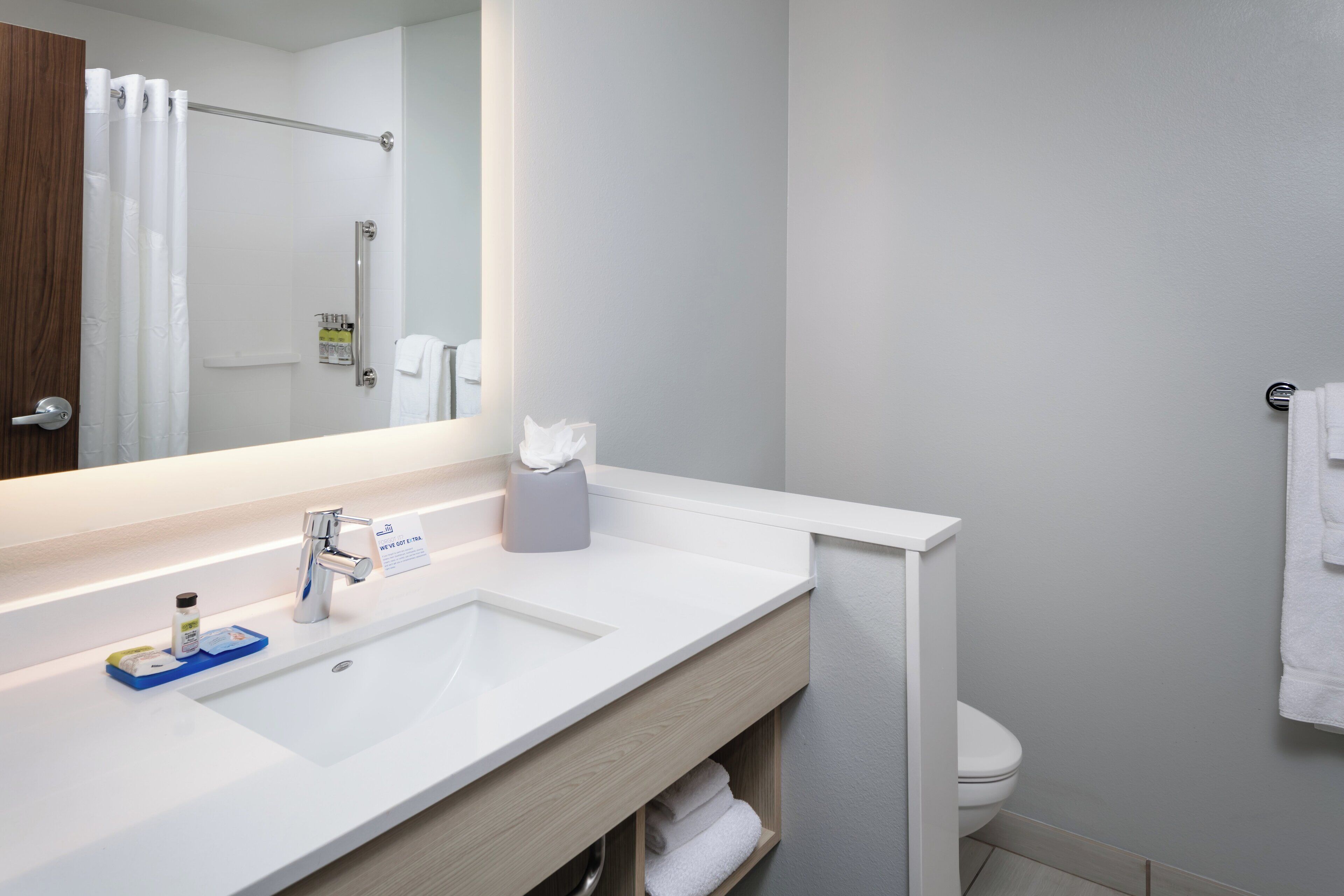A modern bathroom with a white sink, a mirror, a towel rack, and a shower area.