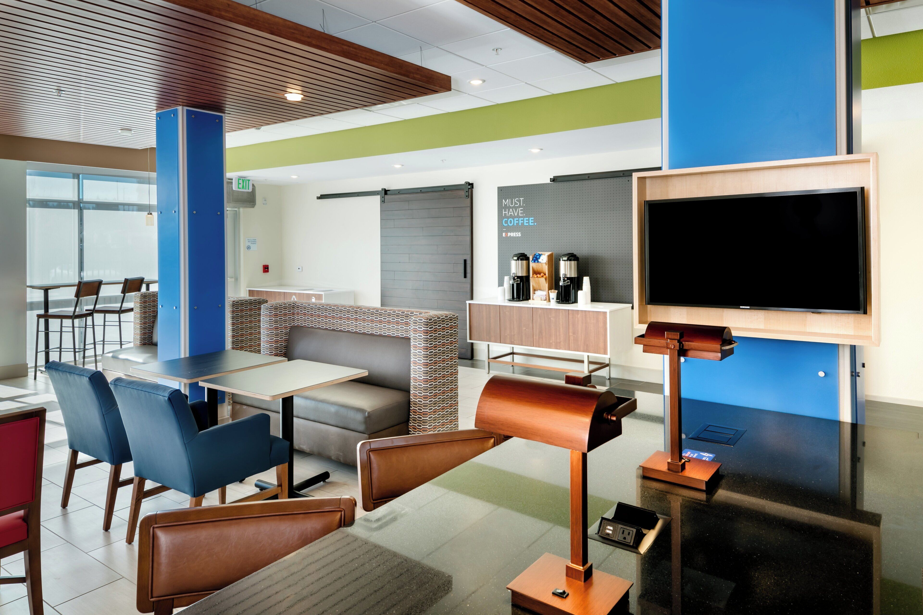 Un moderno vestíbulo de hotel con zonas de estar, una estación de café y un televisor.