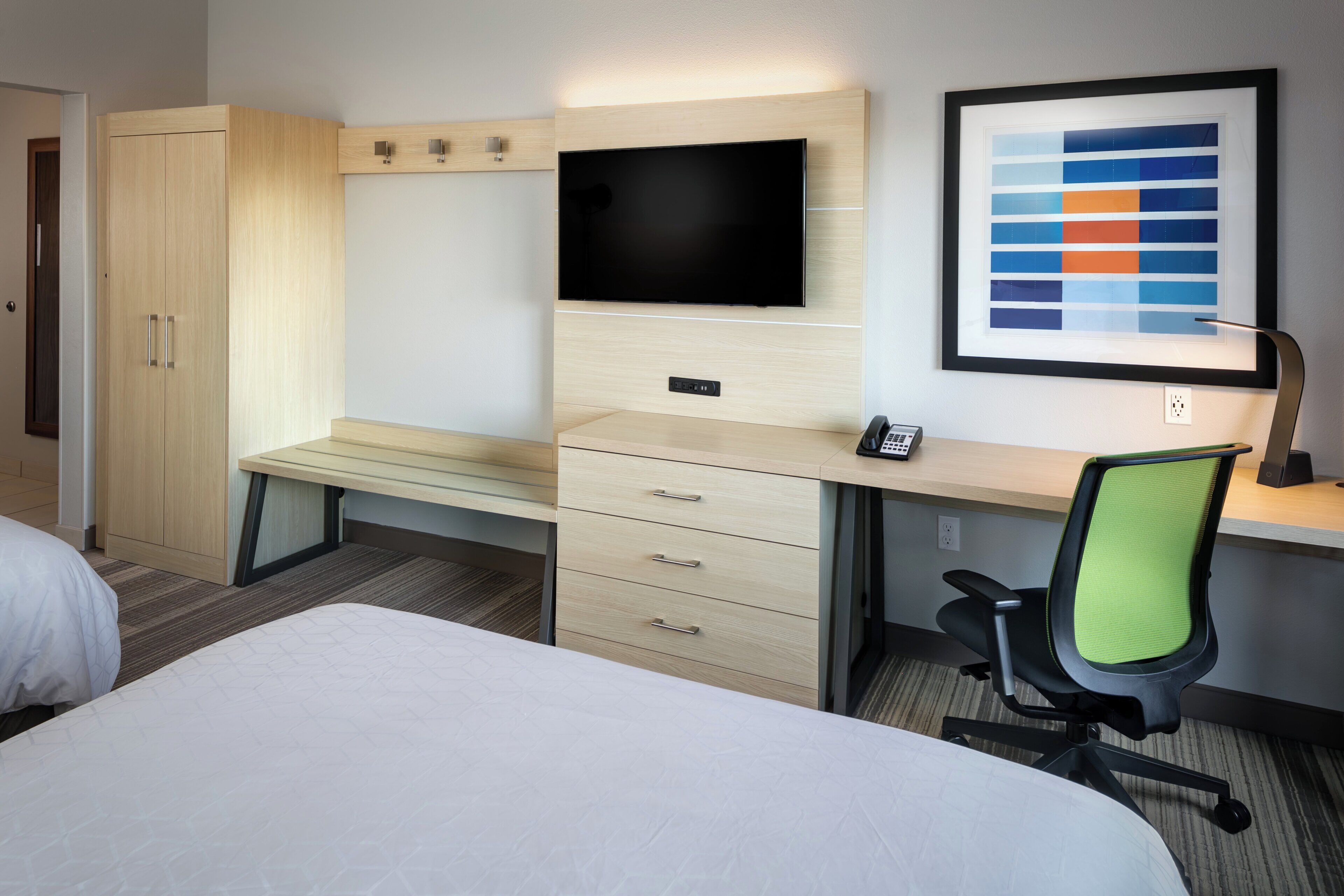 Habitación de hotel con cama, escritorio con silla, televisor y un cuadro en la pared.