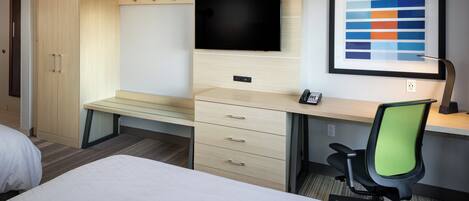 Habitación de hotel con cama, escritorio con silla, televisor y un cuadro en la pared.