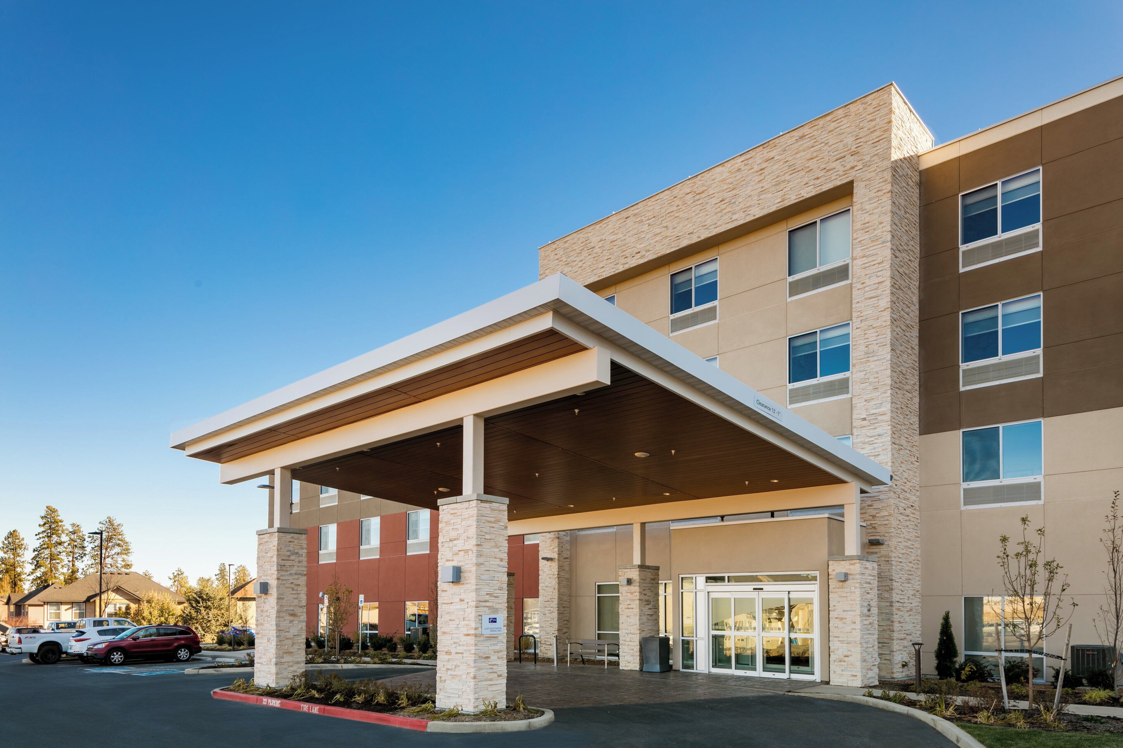 A multi-story hotel with a covered entrance, a parking lot, and a clear sky.