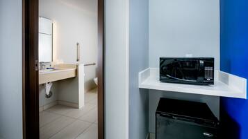A hotel room with a white sink, a microwave on a white shelf, and a black appliance below.