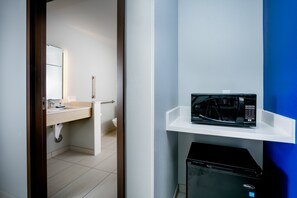 Een hotelkamer met een witte wastafel, een magnetron op een witte plank, en een zwart apparaat eronder.