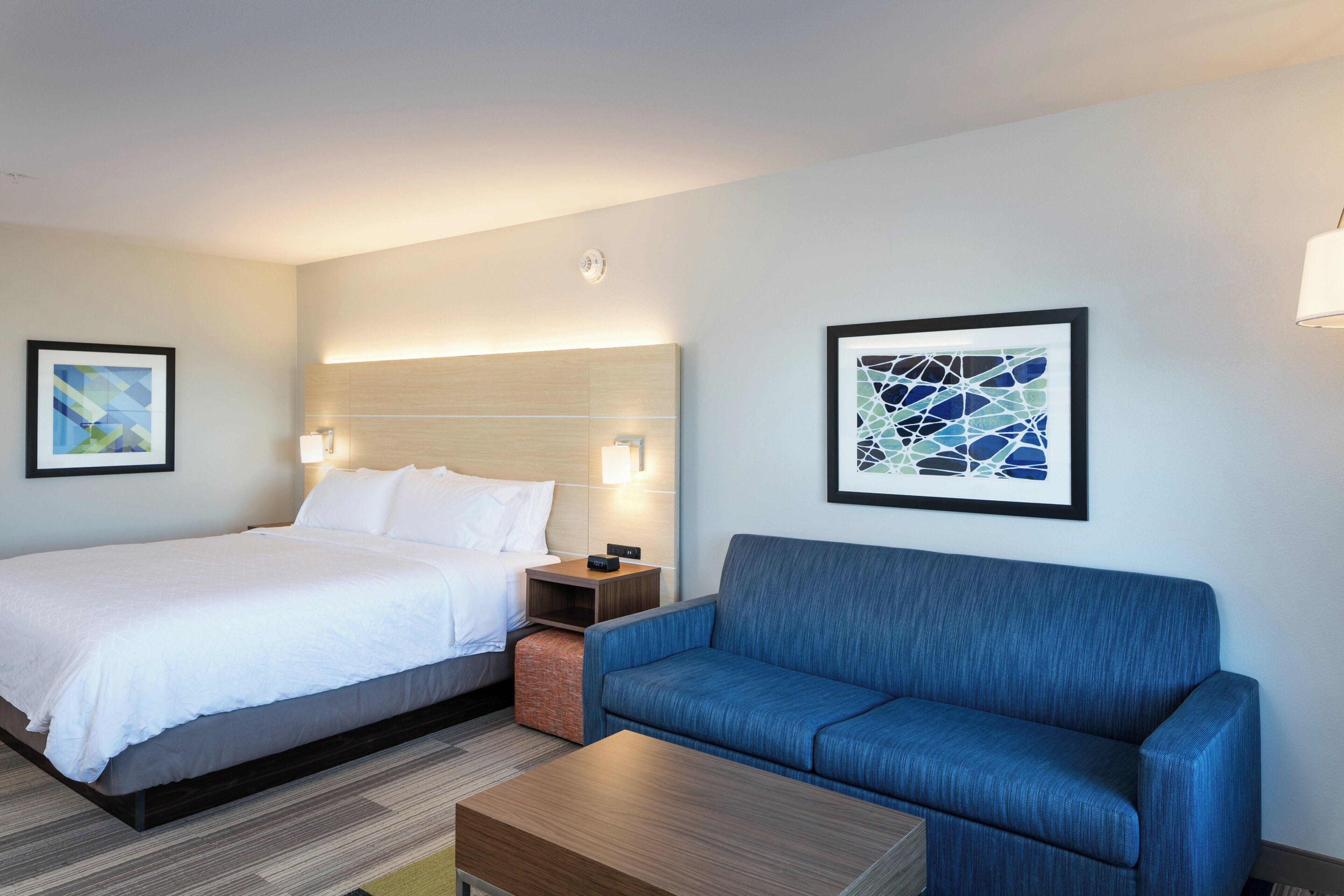 A hotel room with a bed, a blue sofa, a wooden coffee table, and two wall-mounted lamps.