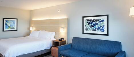 A hotel room with a bed, a blue sofa, a wooden coffee table, and two wall-mounted lamps.