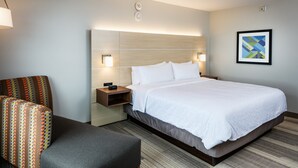 A hotel room with a large bed, a bedside table with a lamp, a chair with a patterned cushion, and a framed abstract artwork on the wall. - Holiday Inn Express & Suites Bend South by IHG (Bend)