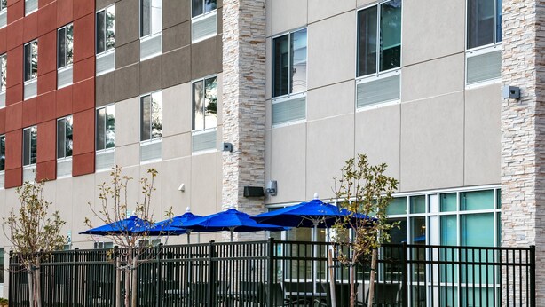 A modern building with a stone facade, multiple windows, and outdoor seating with blue umbrellas. - Holiday Inn Express & Suites Bend South by IHG (Bend)