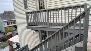 Eine mehrstöckige Holztreppe mit Balkon, die verschiedene Etagen eines Gebäudes mit weißem Putz verbindet.