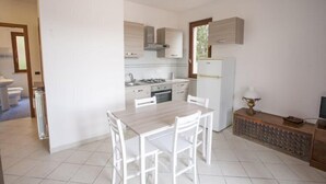 A compact kitchen with white cabinets, a dining table with chairs, and a small refrigerator. - Bilocale Consumella (Portoferraio)