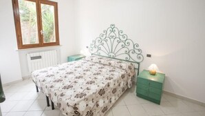 A bedroom with a bed, a nightstand, a green drawer, a window, and a radiator. - Bilocale Consumella (Portoferraio)
