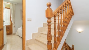 A staircase with wooden balusters and a handrail, leading to a bedroom with a bed and a window with curtains. - BELLA - Chalet with terrace in Port d'Alcúdia. Free WiFi (Alcúdia)