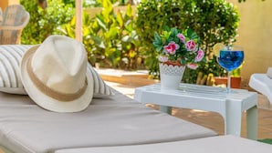 A sun lounger with a straw hat, a potted plant with pink flowers, and a glass of blue drink on a white table. - BELLA - Chalet with terrace in Port d'Alcúdia. Free WiFi (Alcúdia)