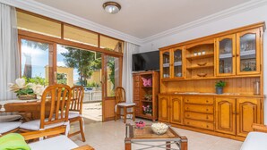 A spacious living area with a dining set, a TV, wooden cabinets, and a view of the outdoors. - BELLA - Chalet with terrace in Port d'Alcúdia. Free WiFi (Alcúdia)