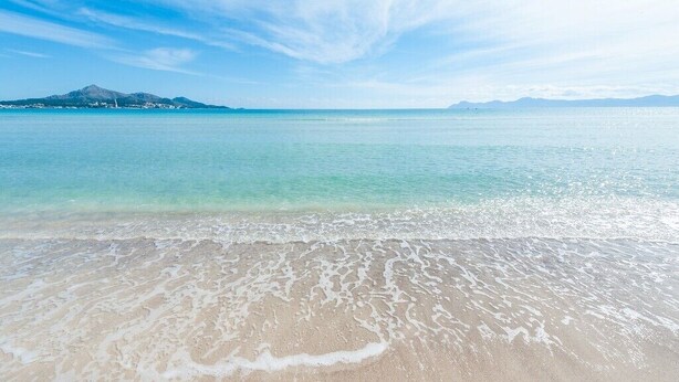 A beach with clear turquoise water and gentle waves, a distant mountain, and a clear sky. - BELLA - Chalet with terrace in Port d'Alcúdia. Free WiFi (Alcúdia)