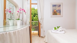 A bedroom with a glass dresser, a bed with white linens, a painting on the wall, and a balcony with curtains. - BELLA - Chalet with terrace in Port d'Alcúdia. Free WiFi (Alcúdia)