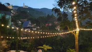 An outdoor dining area with a long table set for a meal, surrounded by trees and string lights. - Le Vent Homestay Tam Dao (Tam Dao)