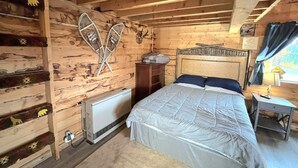 Een knus slaapkamer in chaletstijl met een bed, een dressoir, een radiator en een raam met gordijnen.