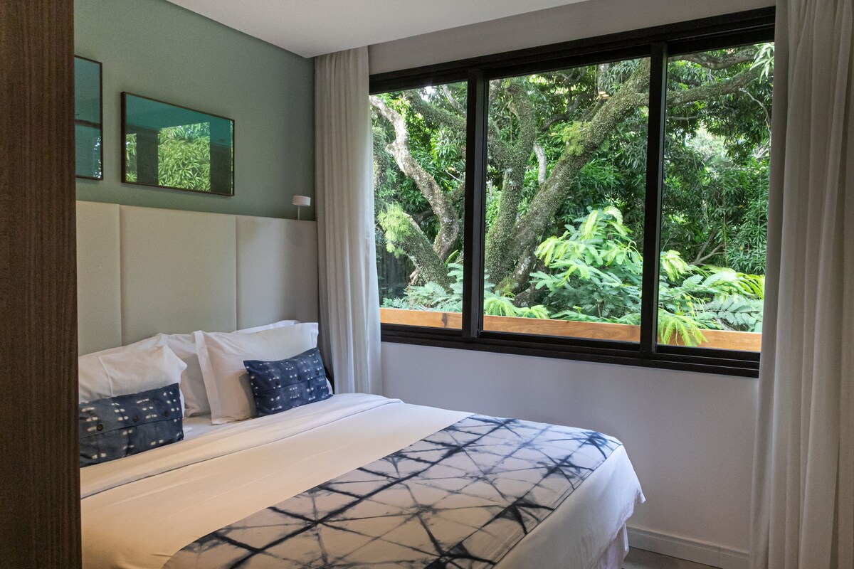 Een slaapkamer met een groot bed, uitzicht op groen door een raam en een hoofdeinde met ingebouwde verlichting.