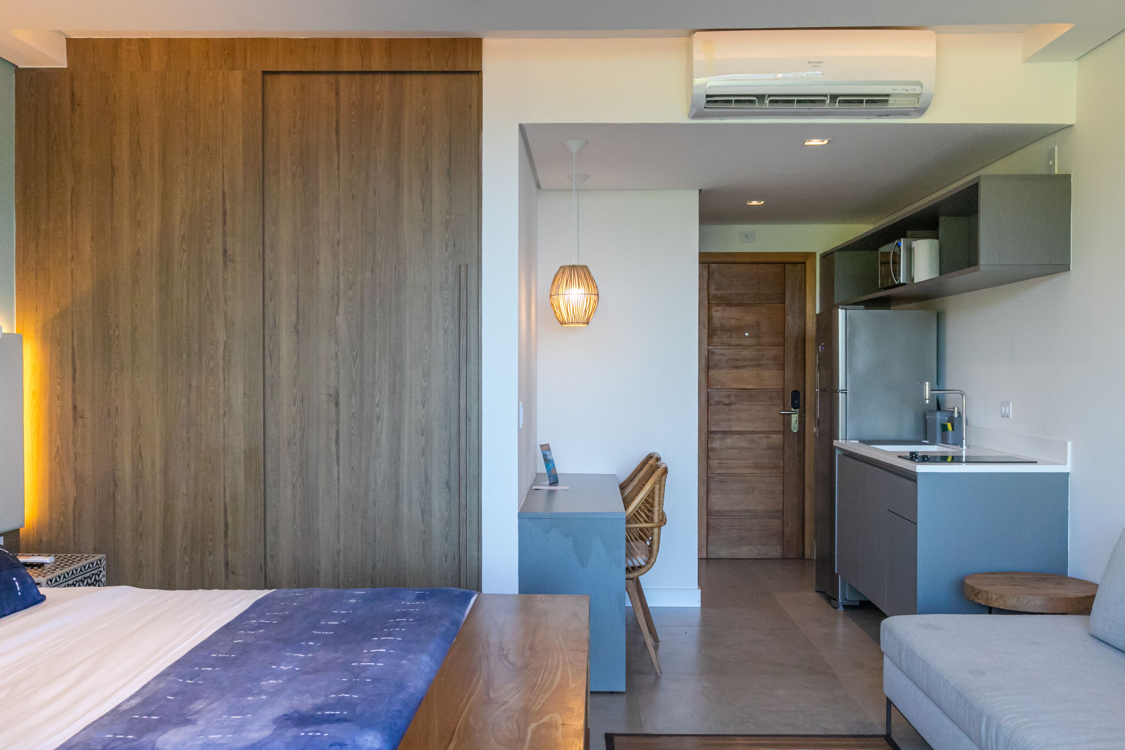 Quarto de hotel moderno com cama, uma pequena mesa de escritório, cadeira, cozinha compacta e área de jantar.