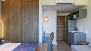 Quarto de hotel moderno com cama, uma pequena mesa de escritório, cadeira, cozinha compacta e área de jantar.