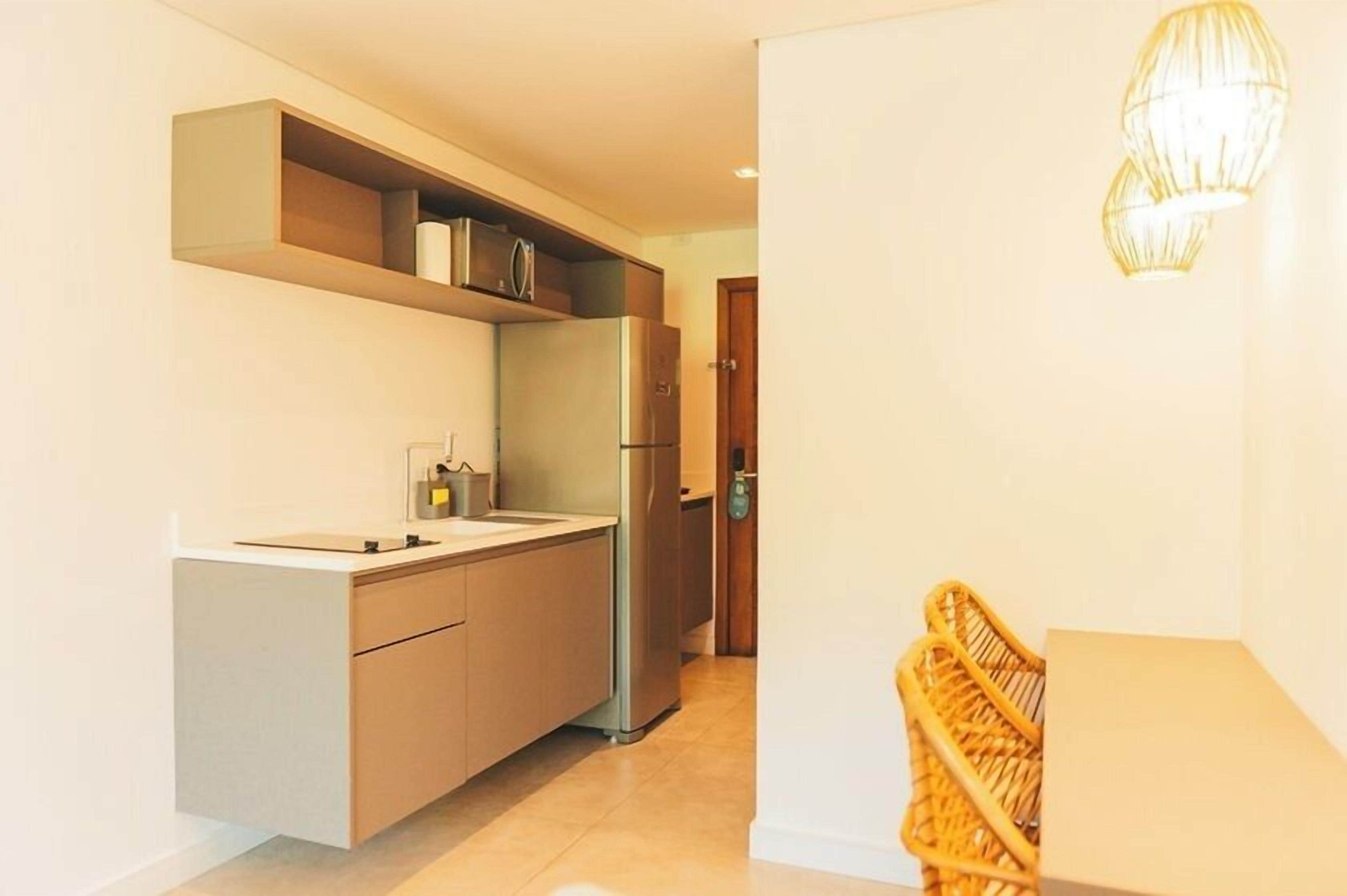 Een moderne keuken met een inbouwkoelkast, een magnetron en een spoelbak. In de hoek staat een rieten stoel en er is een deur naar een andere kamer.