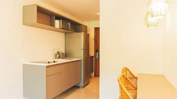 Een moderne keuken met een inbouwkoelkast, een magnetron en een spoelbak. In de hoek staat een rieten stoel en er is een deur naar een andere kamer.