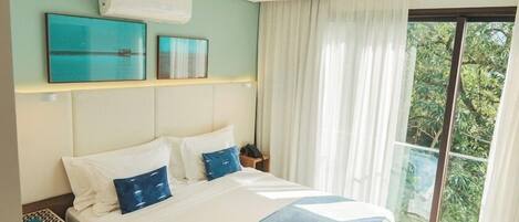 A hotel room with a bed, a nightstand, a wall-mounted air conditioner, and a large window with curtains.