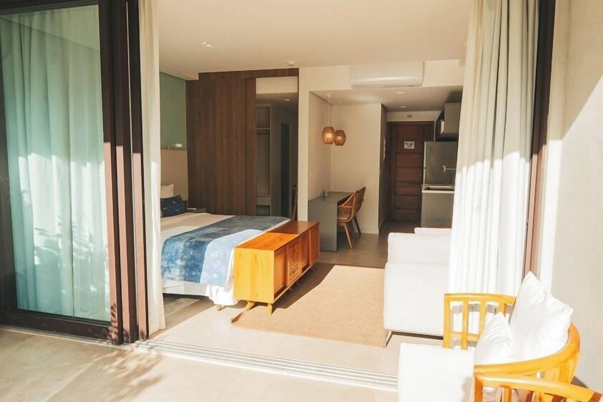 Una habitación de hotel moderna con una cama grande, un rincón de descanso con una silla, una mesita y una kitchenette.