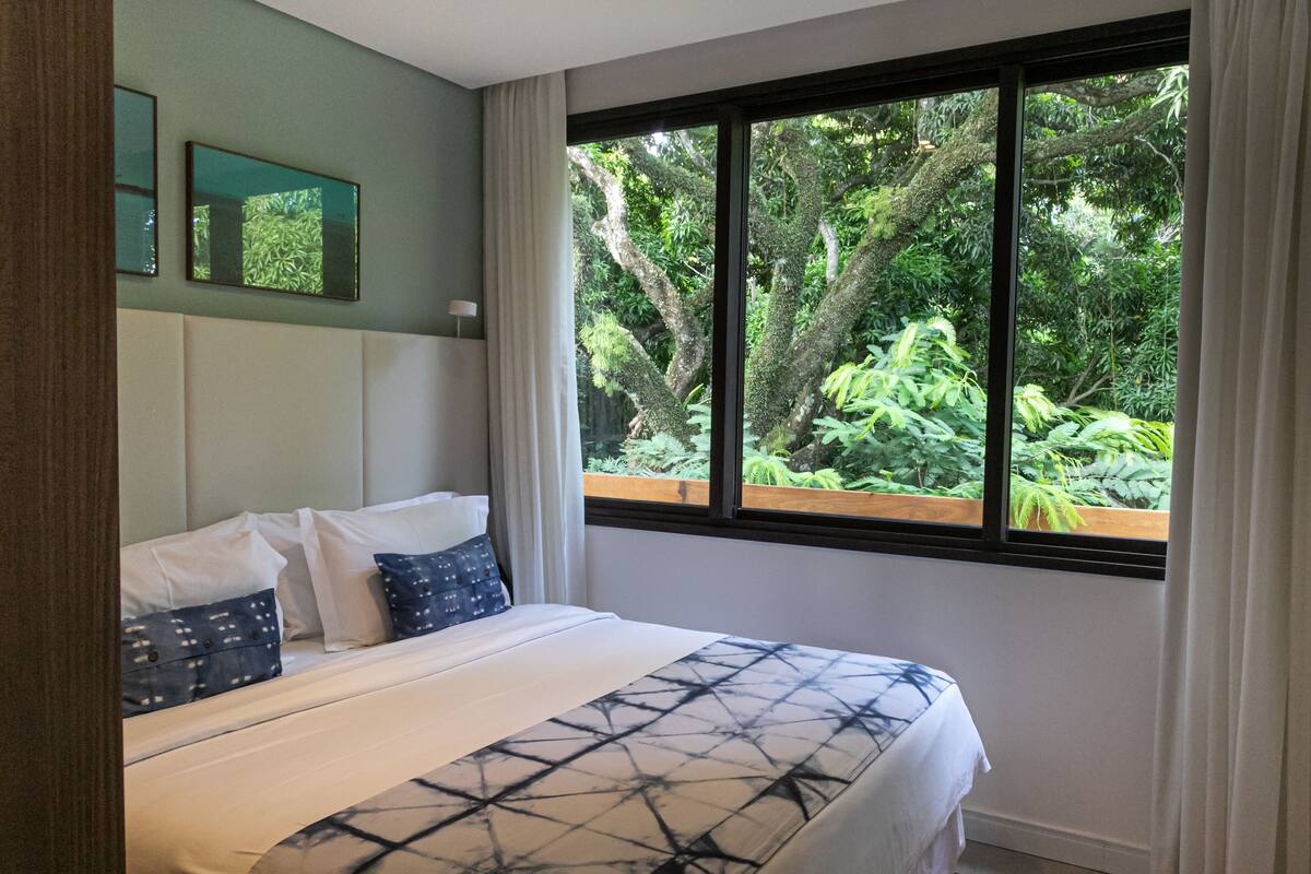 Un dormitorio con una cama grande, cabecera y ventana con vistas a zonas verdes.