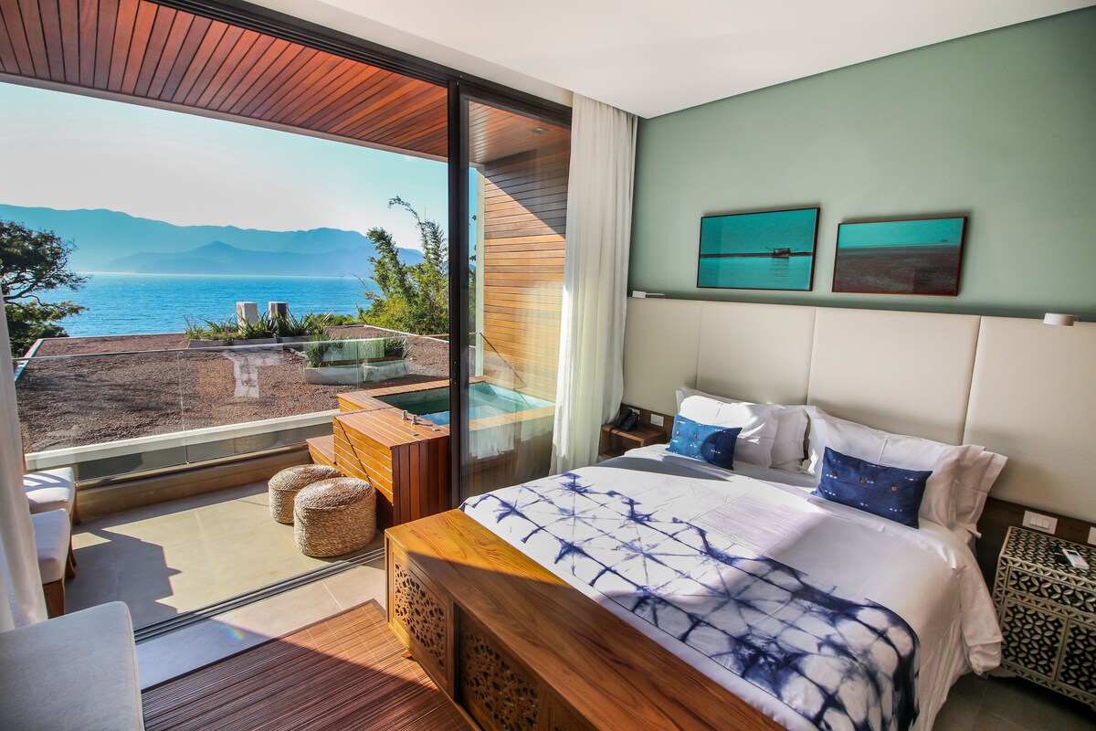 Een slaapkamer met een groot bed, uitzicht op zee en een whirlpool.