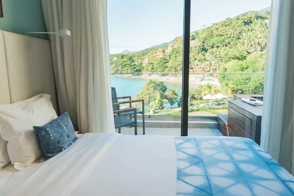 Un dormitorio con cama, una silla y vistas a la playa y colinas.