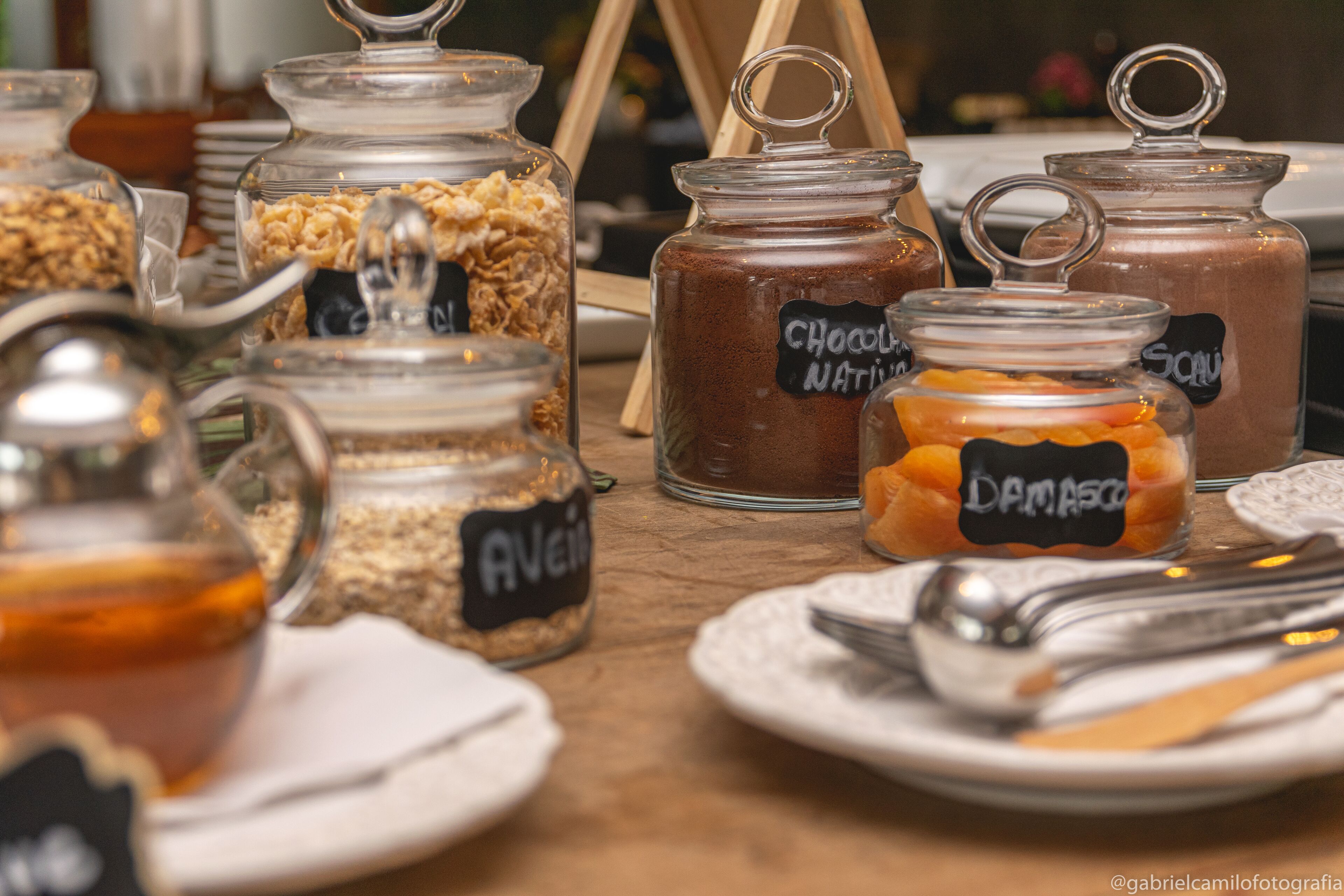 A table with various food items in glass jars labeled with names like "Chocolate Nature," "Damasko," and "Avey."
