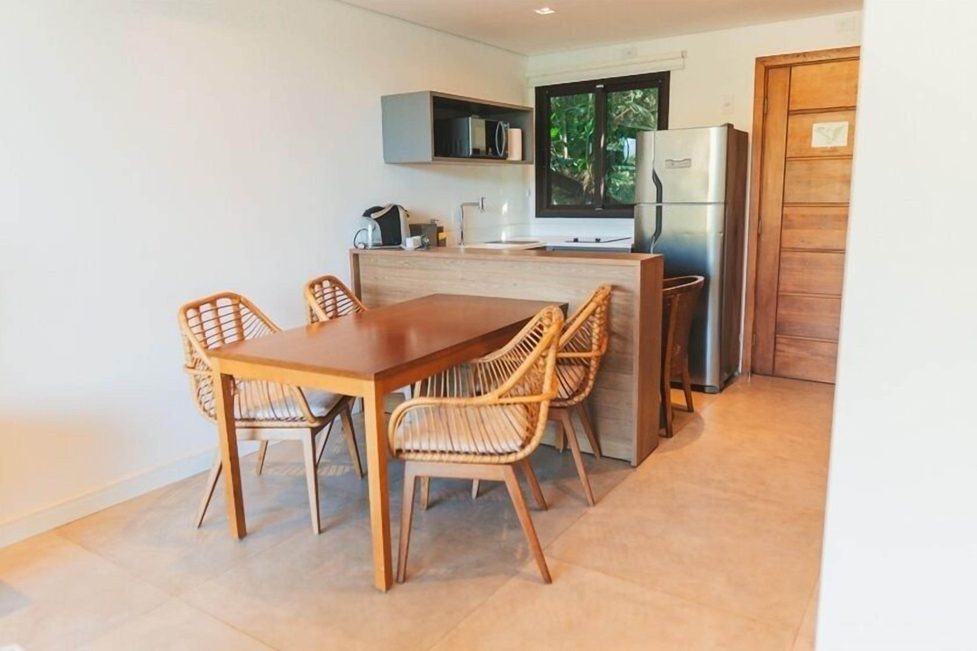 Een kleine keuken met een houten eettafel en stoelen, een inbouwoven en een koelkast.