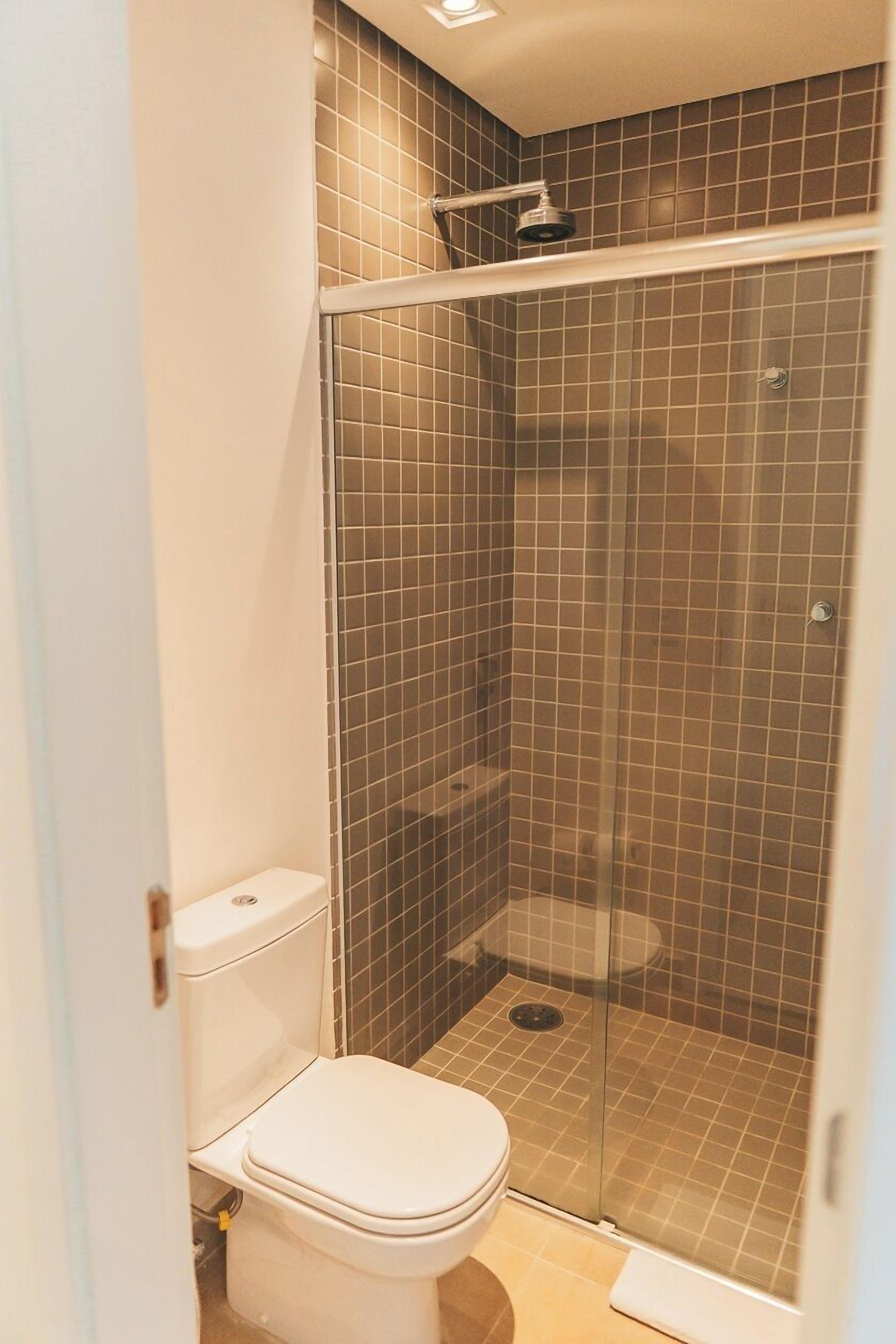 Een kleine, afgesloten douchecel met een glazen deur, een toilet en betegelde wanden.