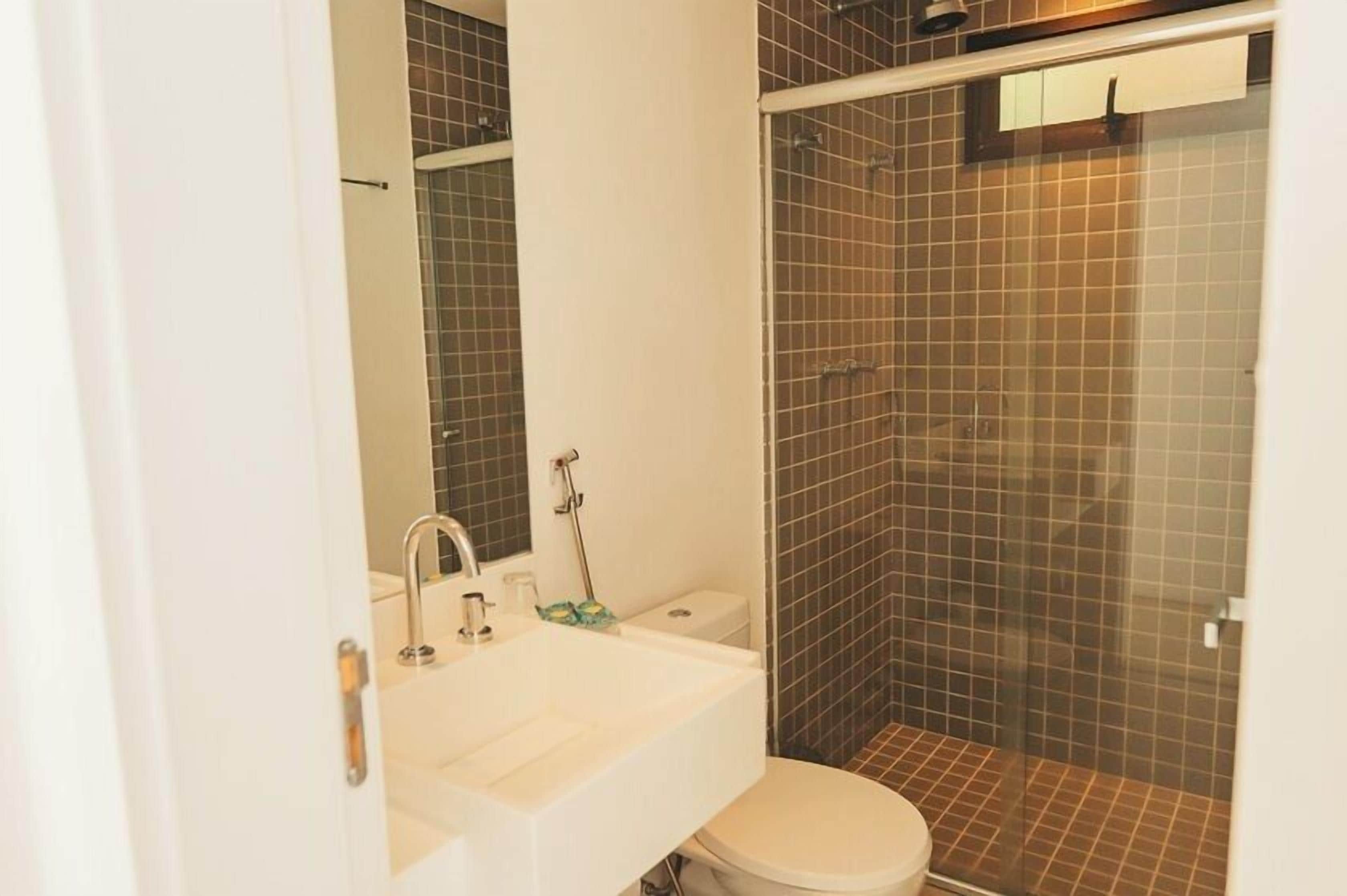 Un bany amb un lavabo blanc, un vàter i una zona de dutxa amb parets de rajola.