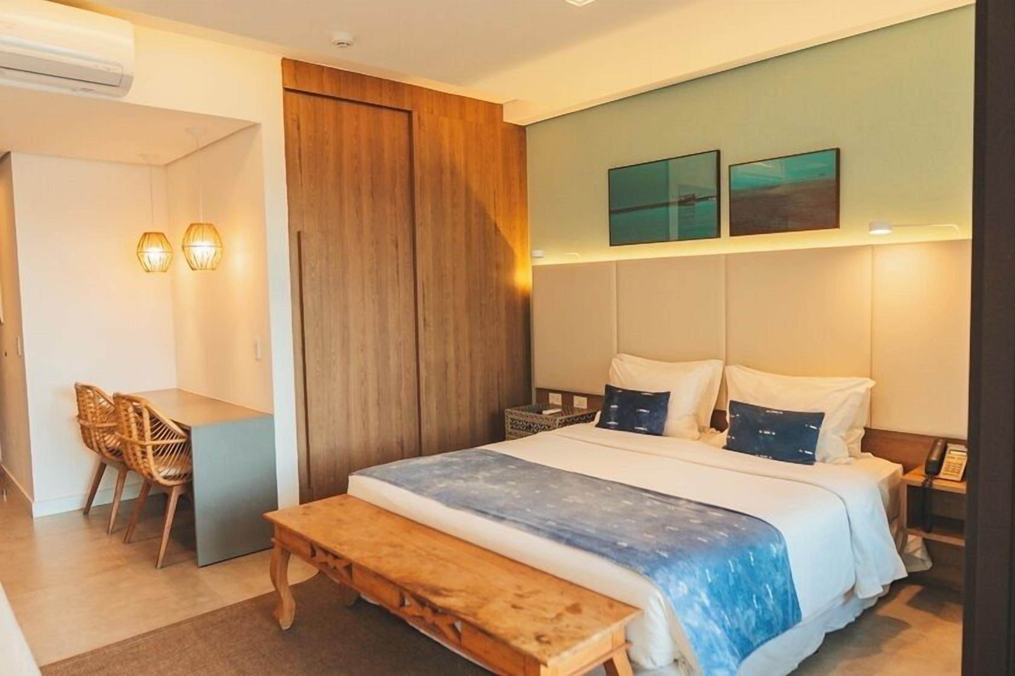 Una habitación de hotel con cama, mesita de noche, lámpara y escritorio con sillas.