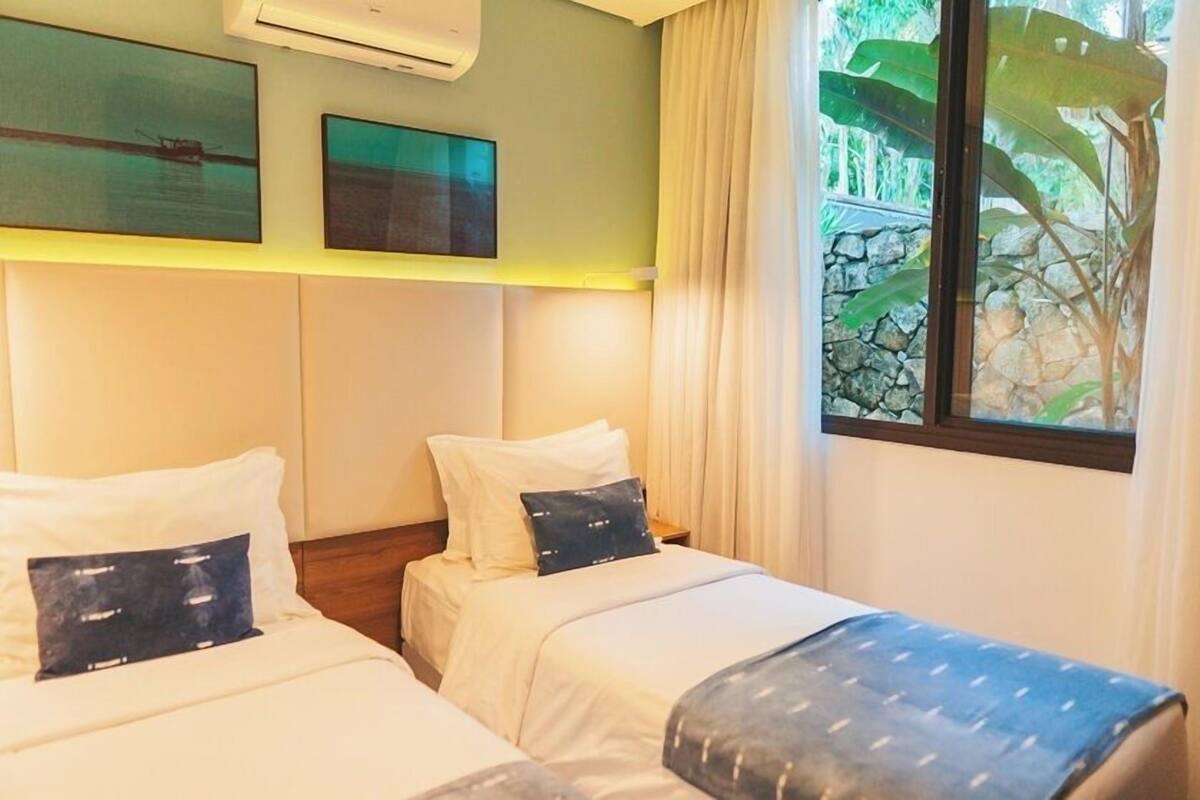 Una habitación de hotel con dos camas, un ventanal con cortinas y cuadros en la pared.