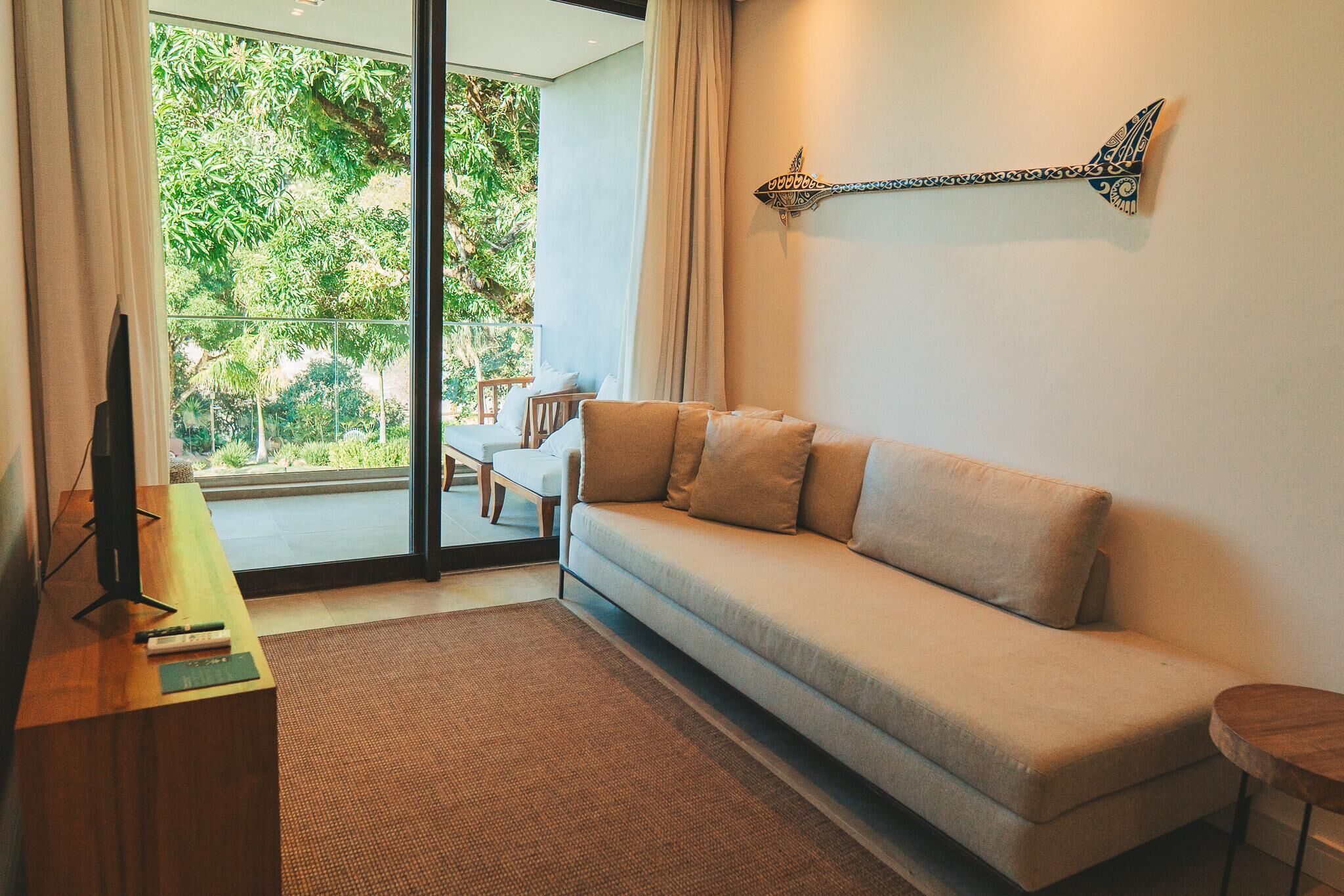 Una sala de estar moderna con un sofá, un televisor y vistas al verde exterior.
