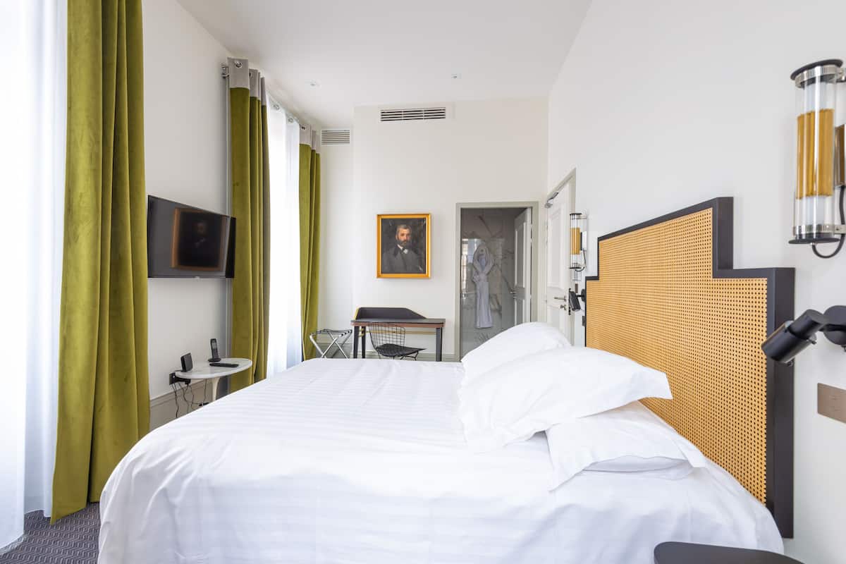 Ein Hotelzimmer mit einem großen Bett, einem Schreibtisch mit Stuhl, einem Fernseher und einem Bild an der Wand.