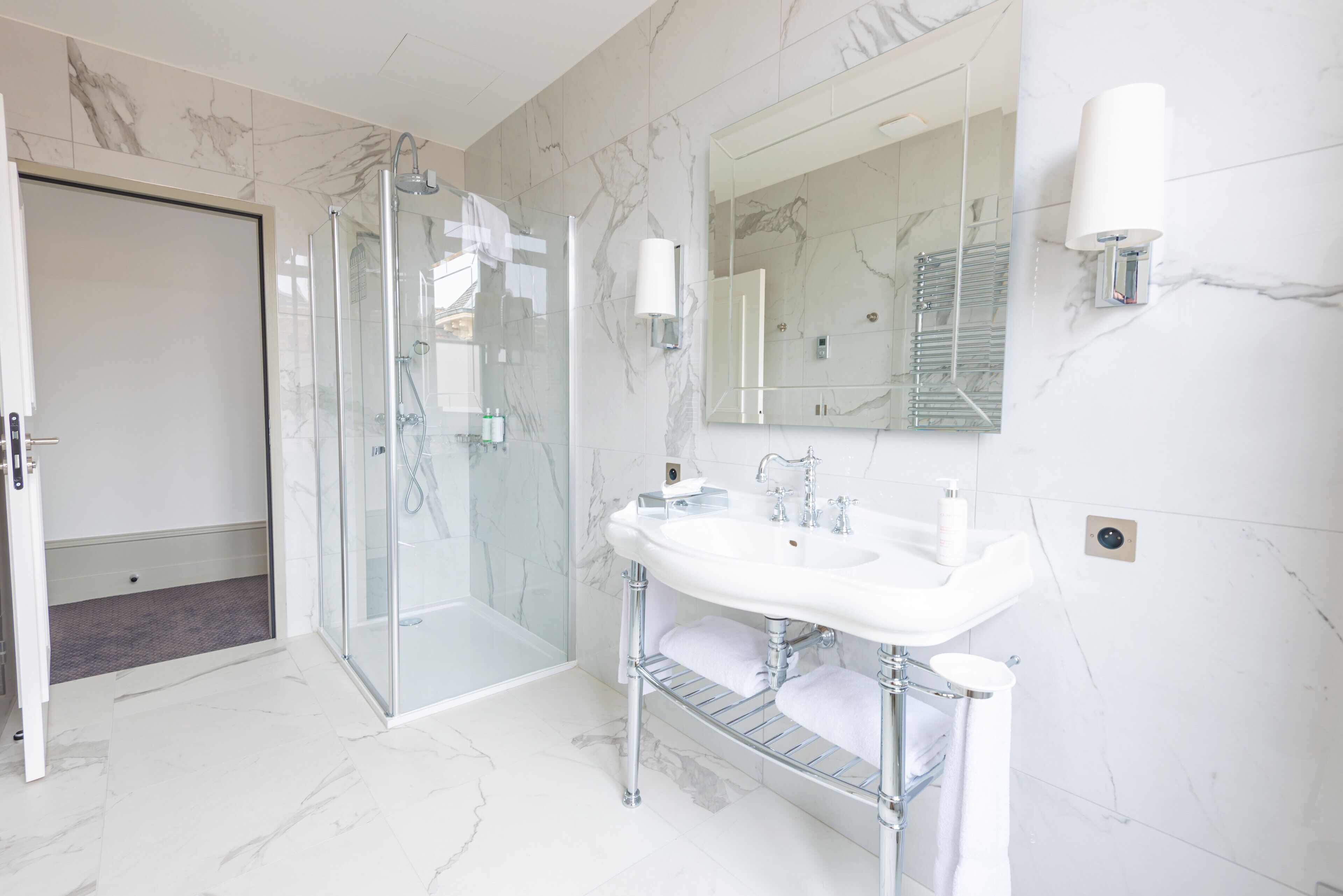 A modern bathroom with a glass shower enclosure, a white sink with chrome fixtures, and a large mirror with wall sconces.